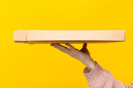 One pizza box in the hand of a female courier on a yellow background. close-up. cover, backgroundの写真素材