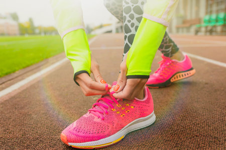 Close-up of a female athlete tying her shoelaces in sneakers before training. Doing sports outsideの写真素材