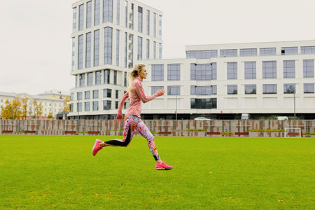 Running training at the stadium. A young woman in a bright tracksuit practicing running techniqueの写真素材