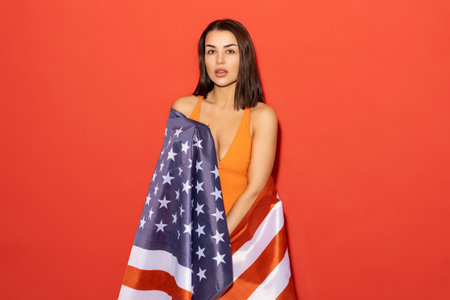 An attractive woman in an orange swimsuit holds an American flag on a red background. The concept of...
