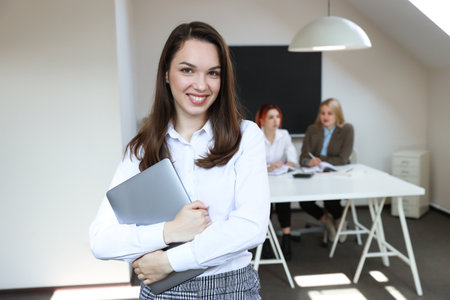 Portrait of a woman with a laptop on the background of a working office.Working office environmentの写真素材