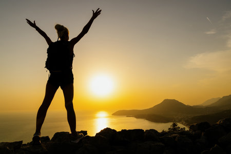 The silhouette of a joyful woman with her hands raised while hiking at sunset. beautiful sceneryの写真素材