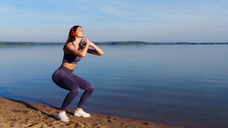 A young woman in a tracksuit squats during a workout outside in the morning in the summerの写真素材
