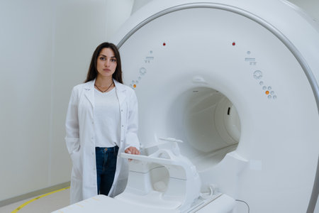 A young female doctor in a white coat stands next to a magnetic resonance imaging machine....
