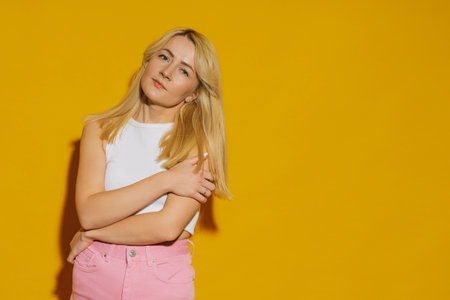 The model poses in the studio on a yellow background. A young woman in a white top and pink jeansの写真素材