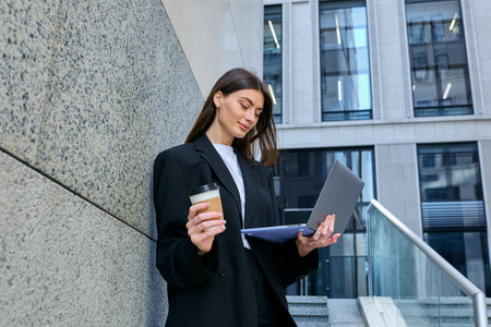 Businesswoman, laptop in hand, works on-the-go in her suit amidst the hustle and bustle of the...