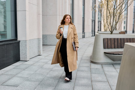 The urban landscape, businesswoman adorned in a fashionable trench coat, navigates the city's...