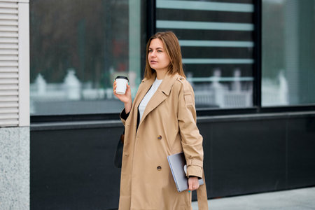 A modern businesswoman, outdoors in her fashionable trench coat, taking a breather from her busy schedule