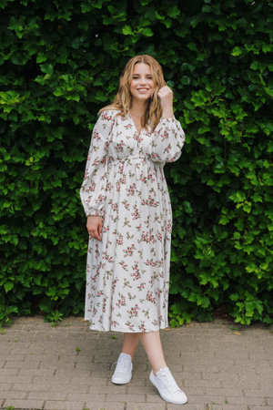 A young woman in a dress on the background of a green hedge. The model poses in summer in good...