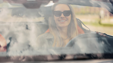 A smiling woman is sitting in her new convertible car. Successful woman, summer vacation