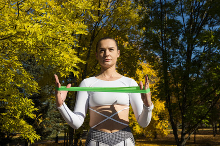 Portrait of an athlete who trains using a fitness elastic band. A woman trains in a city park.の写真素材