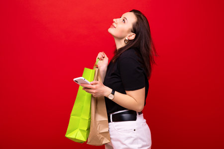 A young woman with a shopping bag and a phone in her hand on a red backgroundの写真素材