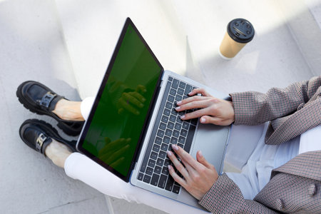 Close-up of the hands of a woman who is working on a laptop outside. Freelance and office anywhere. Mockup, green screenの写真素材
