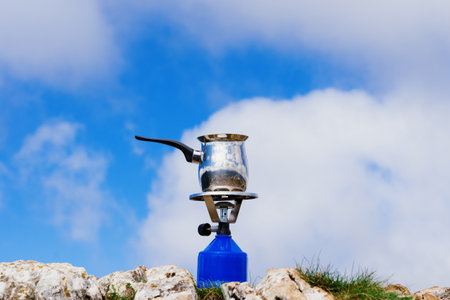A portable gas burner with a pot stands on the rocks against the sky. Cooking during a hikeの写真素材