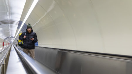 A red-bearded courier with a yellow backpack goes to pick up an order in the subway crossing. The courier looks at the order data in the phoneの写真素材