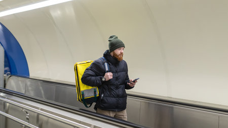 A courier rides an escalator in the subway with a mobile phone. Pizza delivery in the cityの写真素材