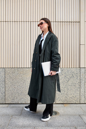 Stylish young freelance woman dressed in a black raincoat over a blouse enjoys the freedom of walking around the city.