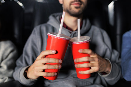 Close-up of two red cups with soda in the hands of a man who came to the cinema. Food and drinks at...