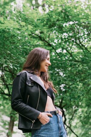 Portrait of a young woman. Leather jacket and jeans, the model poses against a background of green...
