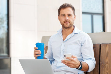 A successful businessman sits on a bench on the street and works at a laptop during a break.の写真素材