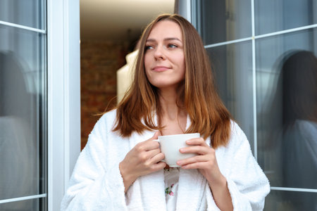 A young woman is resting in a hotel. A model in a white bathrobe drinks coffee on the balcony.の写真素材