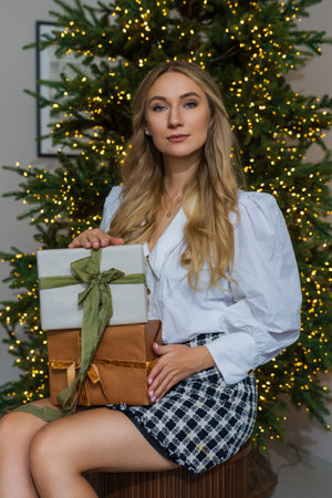 Young slender woman with blond hair holds a box with a ribbon on the background of the Christmas tree.の写真素材