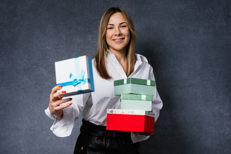 Attractive young woman in a white shirt with boxes of Christmas gifts on a dark backgroundの写真素材