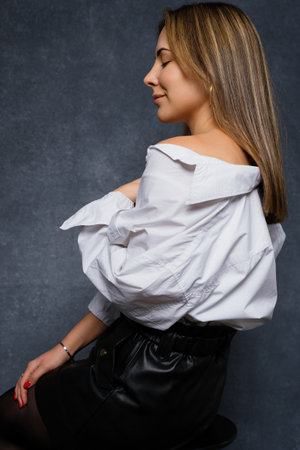 A young woman in a white shirt is sitting on a chair in the studio. Fashion shooting for a businesswomanの写真素材