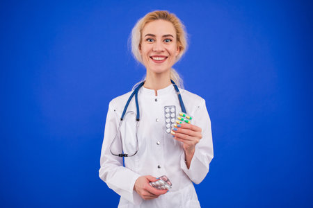 Smiling nurse holds pills in her hands on a blue background.の写真素材