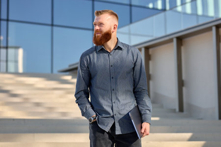 Well-groomed European man with a red beard is waiting for a business partner while standing on the...