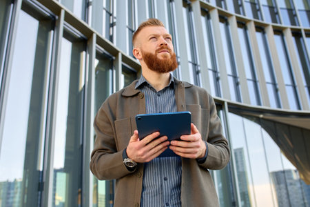 A 35-year-old man with a red beard holds a tablet in his hands and checks the area around him.の写真素材