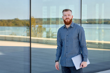Successful aspiring businessman man with red beard enjoys warm weather while walking around the city.の写真素材