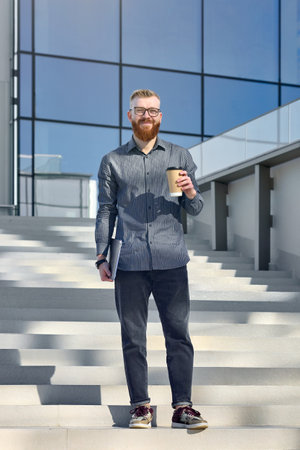 Successful aspiring businessman man with red beard enjoys warm weather while walking around the city.の写真素材