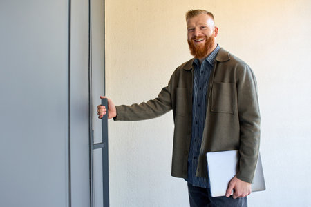 Business man with a red beard stands at the entrance to the building.