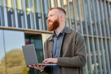 A 35-year-old man with a red beard checks mail from a laptop in his hands while walking down the street.の写真素材