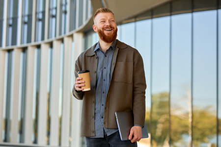 A 35 year old man with a red beard walks around the city and drinks coffee during his lunch break in the office.の写真素材