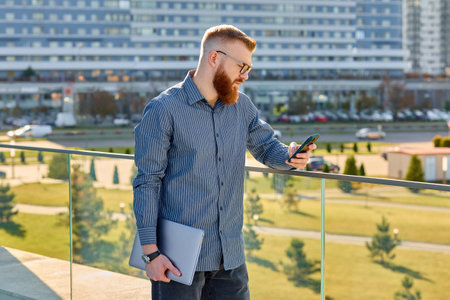 Handsome red-haired freelancer man with a beard checks mail while walking around the city.の写真素材