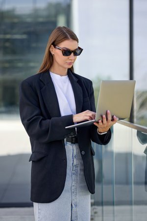 Confident stylish young woman goes outside with a laptop during a coffee break in the office.の写真素材