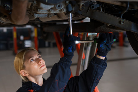 A young female car mechanic unscrews the bolts in the suspension of a car that is on a lift against the background of a service centerの写真素材
