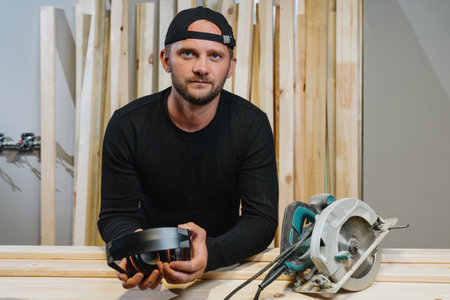 Portrait of a carpenter man who holds headphones in his hands against noise, tools are lying nearby. Home Workshop.の写真素材