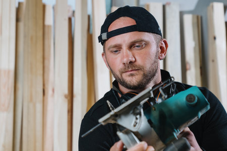 Portrait of a carpenter man in dark clothes holding a circular saw in his hands against the...