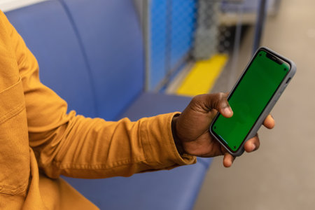 Close-up of the hand of an African-American man with a mobile phone in his hand against the background of public transportの写真素材