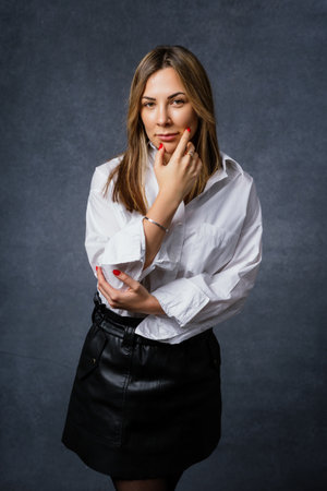 Portrait of a stylish business woman in a white shirt and skirt on a dark background. The model looks into the cameraの写真素材