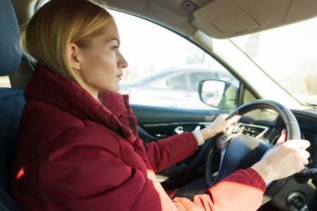 A beautiful young woman in a red jacket is driving a car.の写真素材