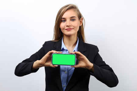 Caucasian fair-haired young woman in a jacket shows a green screen of a smartphone for advertising.の写真素材