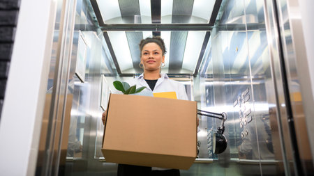 A young woman with a box is standing in an office elevator.