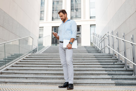 Successful boss man on the background of the stairs with a laptop and smartphone in his hands.