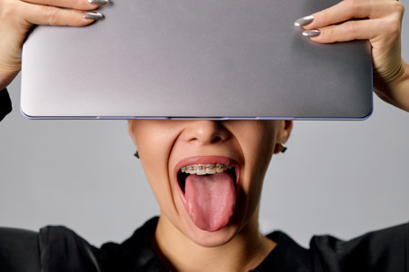 Cute cute woman with braces makes faces and holds a laptop in her hands.