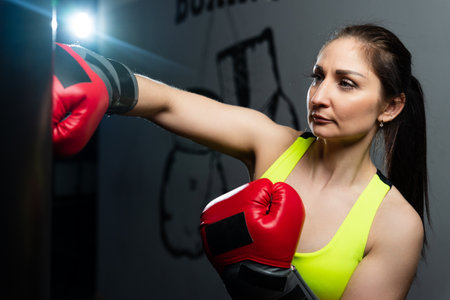 A young woman in a bright tracksuit practices punches on a punching bagの写真素材