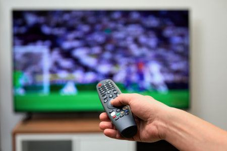 A man watches football and switches TV programs with the remote control.